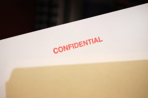 Paper sticking out of a manila folder, labeled confidential in red ink.