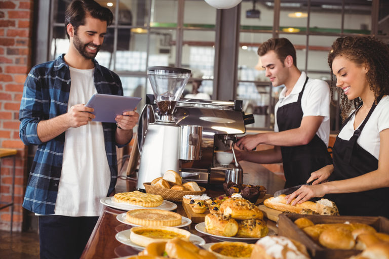 A coffee shop with workers standing behind a counter of pastries, and a customer in front.