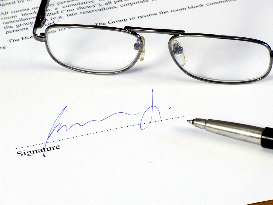 Glasses and a pen sitting on a paper with a signature.